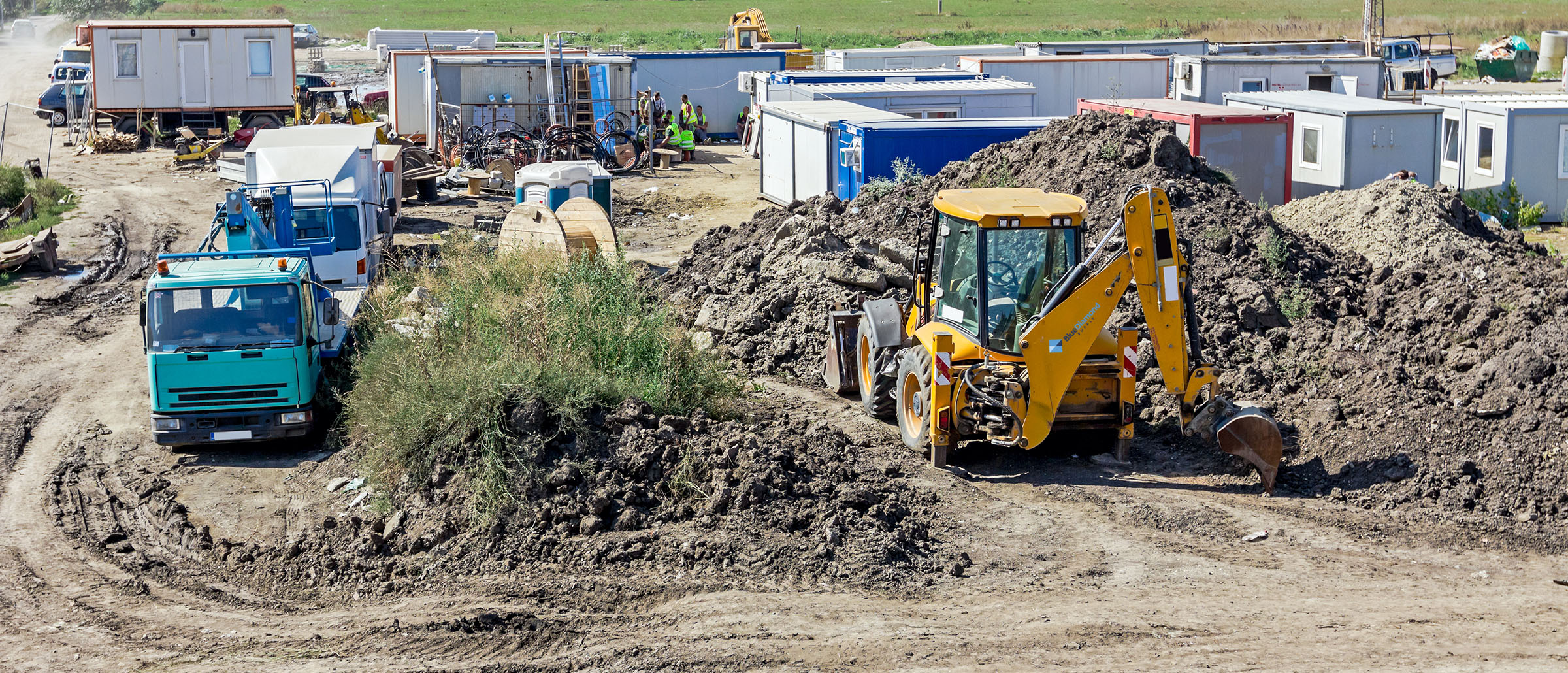 Active jobsite with site trailers, a backhoe and supply trucks